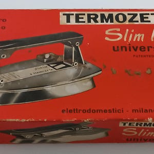 May include: A vintage Termozeta Slim Line iron in its original red box. The box displays the iron's image, product details, and the text "ferro da stiro automatico". The iron is silver with a black handle.