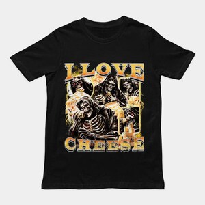 May include: A black short-sleeve t-shirt featuring a graphic print of multiple skeletons eating cheese. The text I LOVE CHEESE is printed in a bold, distressed yellow font above and below the central illustration of the skeletons.