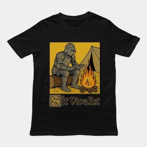 以下が含まれることがあります： 黒の半袖Tシャツ。テントの前で焚き火を囲み、丸太に座る鎧姿の騎士のグラフィックイラストが描かれています。イラストの下には、中世風の装飾的なフォントで「Sir Vivalist」という文字がプリントされています。