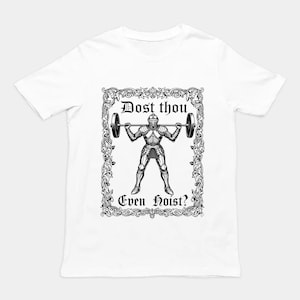 May include: A white short-sleeve t-shirt featuring a black graphic print of a knight in full armor lifting a barbell. The design is enclosed in an ornate rectangular frame and includes the text "Dost thou Even Hoist?" in a gothic font.