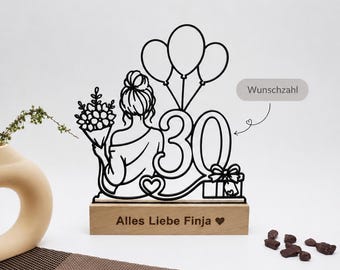 May include: A black wire-frame decorative topper featuring a person holding a bouquet, three balloons, the number 30, and a gift box, mounted on a rectangular wooden base engraved with the text Alles Liebe Finja and a heart symbol.