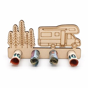 Wohnmobil-Geldgeschenk aus Holz mit vier Geldscheinen vor Nadelbäumen, leicht seitlich.