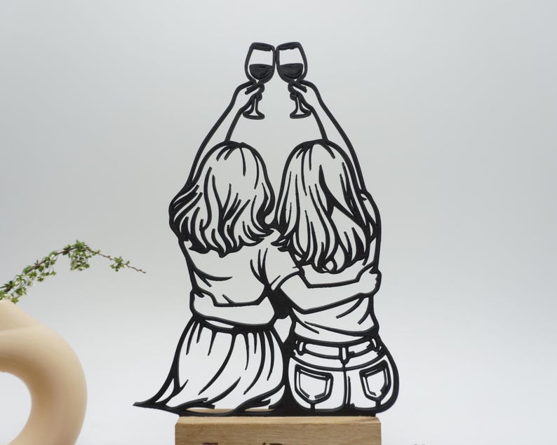 May include: Black silhouette of two figures toasting wine glasses. The figures are embracing, with their backs to the viewer. The artwork is mounted on a wooden base, suggesting a decorative item or a gift.
