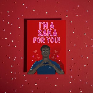 May include: A red Valentine's Day card with a photo of a man making a heart shape with his hands. The text on the card reads "I'm a Saka for you!" in pink letters.