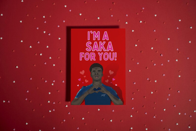 May include: A red Valentine's Day card with a photo of a man making a heart shape with his hands. The text on the card reads "I'm a Saka for you!" in pink letters.