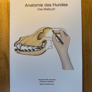 May include: A white book cover with the title "Anatomie des Hundes" and the subtitle "Das Malbuch". The cover features a detailed illustration of a dog's skull with a hand holding a pencil, drawing on the skull.