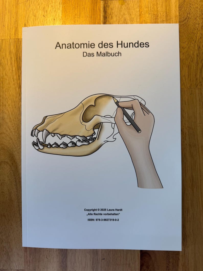 May include: A white book cover with the title "Anatomie des Hundes" and the subtitle "Das Malbuch". The cover features a detailed illustration of a dog's skull with a hand holding a pencil, drawing on the skull.