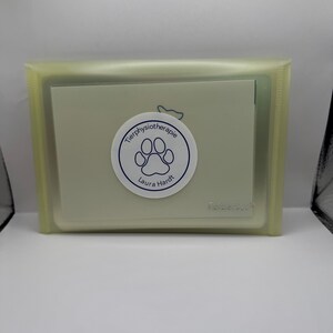 May include: A light green plastic card holder with a white card inside. The card has a blue paw print and the text "Tierphysiotherapie Laura Hardt".