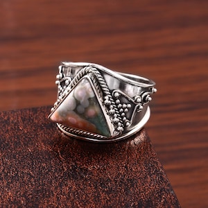May include: A silver ring with a triangular green, pink, and brown gemstone set in a silver band with intricate detailing.
