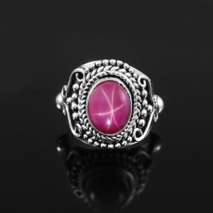 May include: A silver ring with a pink star-shaped ruby gemstone set in a detailed ornate design.