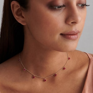 Puede incluir: Un collar de cadena dorada con seis pequeñas piedras preciosas redondas de color rojo vibrante, espaciadas uniformemente y colgando como dijes. La delicada cadena de oro amarillo descansa alrededor del cuello con un diseño sencillo y cierre.