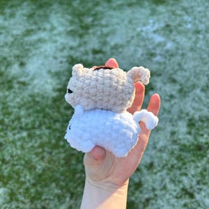 May include: Two crocheted stuffed toys, one white and one beige, are stacked on top of each other. The white toy is on the bottom and the beige toy is on top. The toys are both small and have a rounded shape.