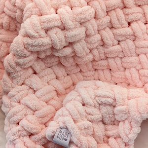 Könnte beinhalten: Eine weiche, rosa gestrickte Babydecke mit gewebter Textur. Die Decke hat ein kleines Etikett mit der Aufschrift "Made with Love".