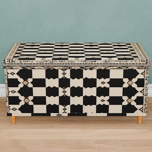 May include: A black and white chequered storage chest with a decorative border. The chest has short legs and is made of wood.