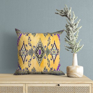 May include: A yellow throw pillow with a purple and blue geometric pattern. The pillow is sitting on a light wood table with two drawers.