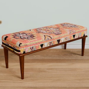 May include: A wooden bench with a colorful patterned cushion. The cushion has a geometric design with shades of pink, orange, and black.