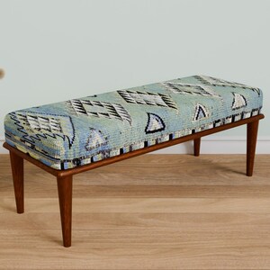 May include: A wooden bench with a blue and white patterned cushion. The bench has a simple design with four legs and a rectangular seat.