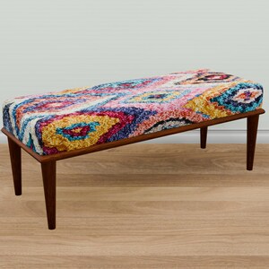 May include: A rectangular upholstered bench with a colorful, patterned top in shades of pink, blue, yellow, and white. The bench has a dark brown wooden frame and four tapered legs. The design is reminiscent of a rug.