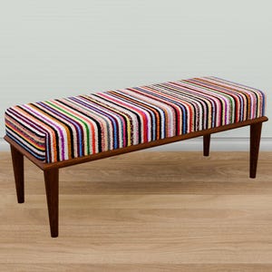 Peut inclure: Un banc rayé coloré avec des pieds en bois. Le banc est recouvert d'un tissu rayé multicolore.