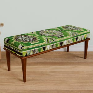 May include: A green and brown patterned bench with wooden legs. The bench is made of fabric and has a geometric design.
