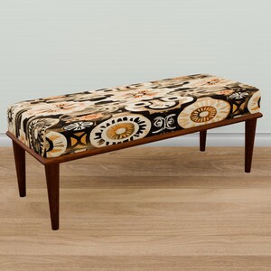 Puede incluir: Un banco de madera con un cojín estampado en marrón, negro y blanco. El banco tiene un diseño sencillo con cuatro patas.