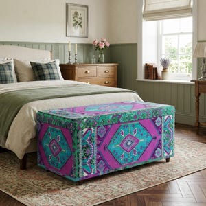 a cozy bedroom with a large bed, a wooden dresser, and a colorful patterned ottoman. The room has a warm and inviting atmosphere, with a window providing natural light and a vase of flowers on the dresser.