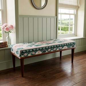 May include: A rectangular upholstered bench featuring a floral pattern in shades of pink, white, and dark green. The bench is supported by four tapered wooden legs in a medium brown finish, providing a stable base for the cushioned seat.