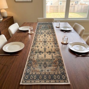 May include: A rectangular table runner featuring a central medallion pattern in shades of cream, navy blue, and muted brown. The textile displays a symmetrical, intricate design with geometric borders and a distressed, weathered appearance.