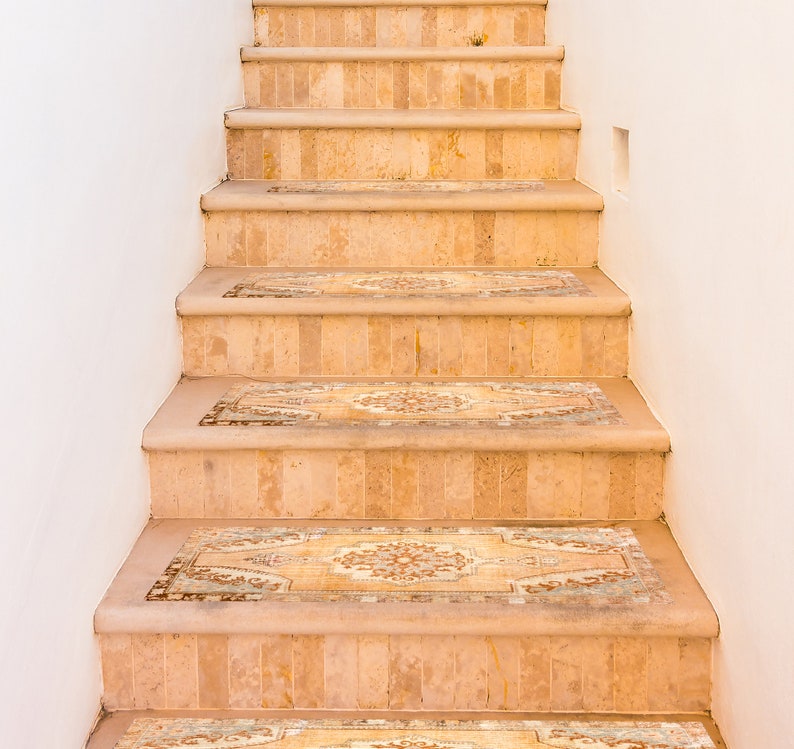 May include: A set of beige stairs with patterned tile insets. The stairs are made of stone or ceramic tile and have a light brown colour. The patterned tile insets are a lighter shade of brown with a floral design.