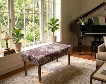 May include: A rectangular upholstered bench featuring a dark red, cream, and black patterned fabric with a geometric design. The bench is supported by four tapered wooden legs and is positioned in a room with a large window and a black grand piano.