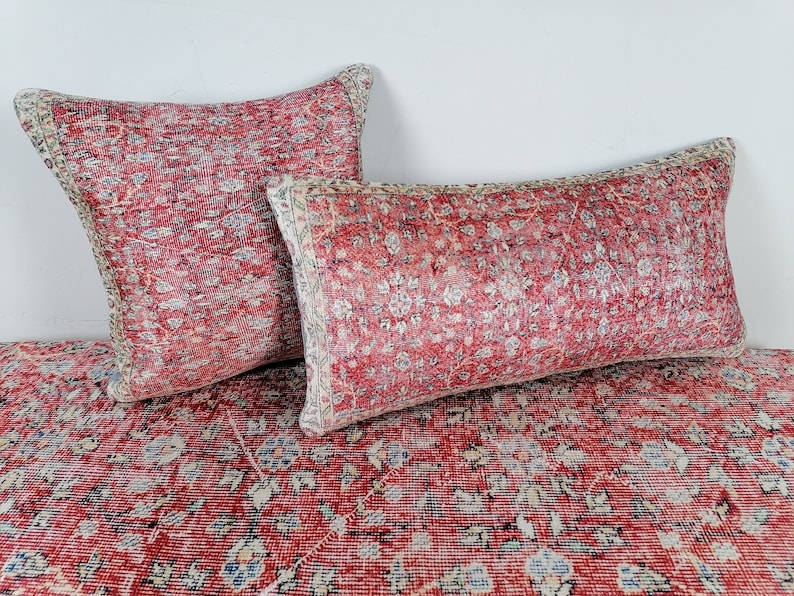 May include: Two red and white patterned throw pillows with a floral design. The pillows are on a red and white patterned rug.