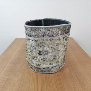 Peut inclure: Un panier de rangement cylindrique en tissu tissé avec un motif bleu et vert. Le panier est posé sur une surface en bois.