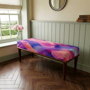 Può includere: Una panca rettangolare con quattro gambe in legno marrone scuro e una seduta imbottita rivestita in un tessuto vivace con un motivo astratto di forme geometriche e linee strutturate nei toni del rosa, viola e blu.