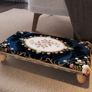 Peut inclure: Un repose-pieds rectangulaire avec un motif floral bleu foncé et un motif ovale central avec des fleurs roses. Le repose-pieds a quatre courtes jambes en bois de couleur claire et une bordure dorée.