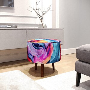 May include: A round ottoman featuring a vibrant, multi-coloured abstract pattern with swirls of bright pink, deep blue, orange, and purple. The seat is supported by three short, dark brown wooden legs, providing a stable base for the circular cushion.