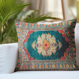 Puede incluir: Un cojín cuadrado con un estampado detallado de una alfombra con motivos en azul verdoso, rojo y amarillo. El diseño incluye un medallón central rodeado de complejos bordes geométricos y florales, imitando un tejido textil.