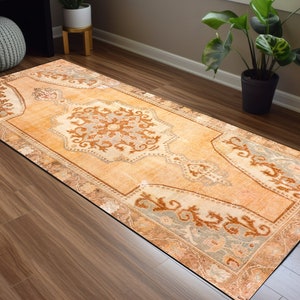 Puede incluir: Una alfombra de pasillo de estilo vintage con un fondo naranja claro y un patr&oacute;n floral detallado en tonos marrones, beige y grises. La alfombra tiene un borde con flecos.