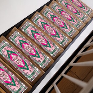 Op de afbeelding: Een set roze en groene getrapte treden met een geometrisch ontwerp. De treden zijn gemaakt van hout en hebben een zwarte rand.