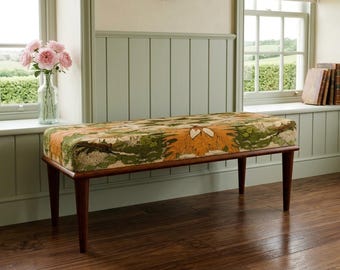 May include: A mid-century style bench with a floral patterned cushion in shades of green and orange. The bench has a dark wood frame and legs. The bench is placed in front of a window.
