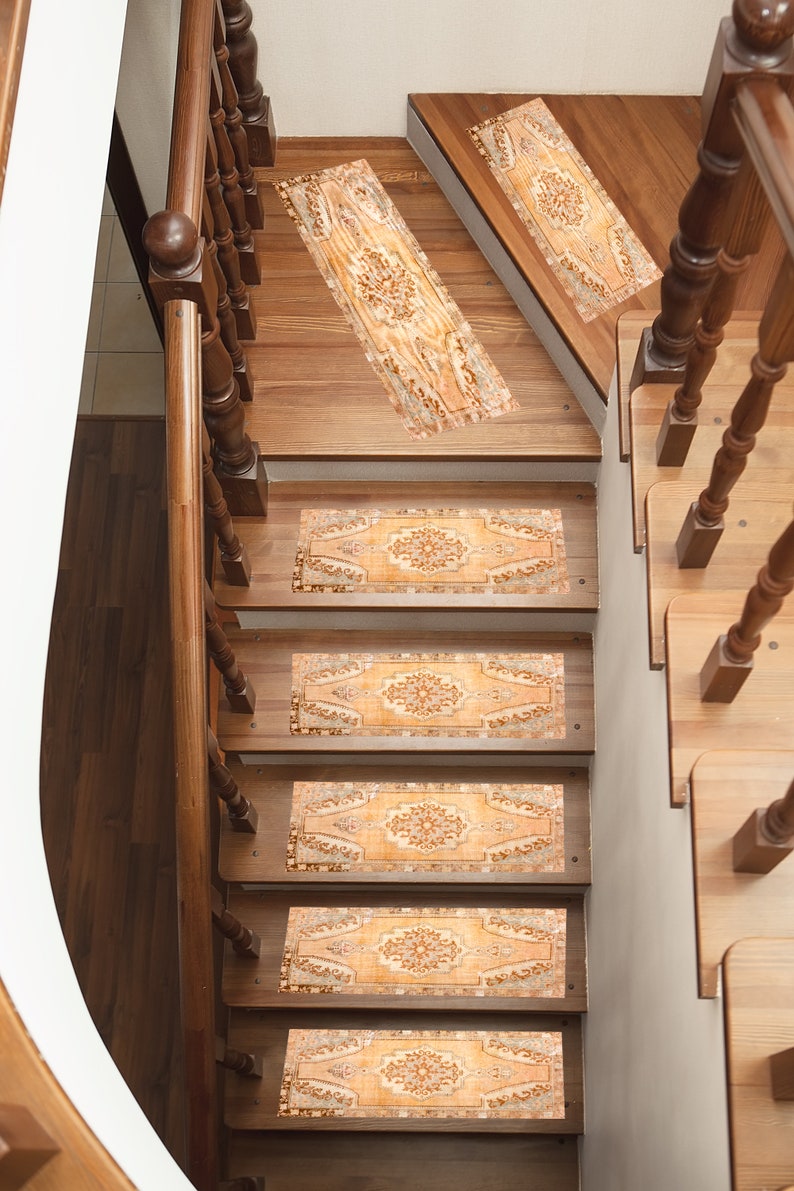 May include: A set of five beige and brown patterned stair treads with a floral design. The treads are placed on a wooden staircase with a wooden handrail.
