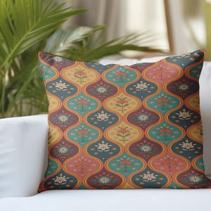 May include: Decorative throw pillow with a repeating floral pattern in shades of teal, orange, yellow, and burgundy. The pillow is placed on a white sofa, with a brown pillow to the right and greenery in the background.