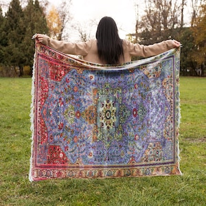 May include: A woman is holding a large, colourful rug with intricate patterns in shades of red, blue, green, and yellow. The rug has a fringed edge and is spread out in front of her.
