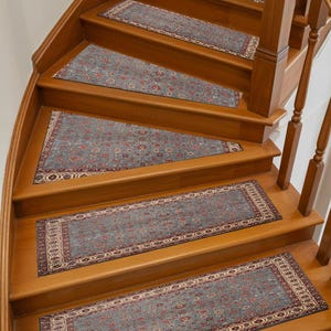May include: A set of stair treads with a traditional Persian rug design. The treads are a muted blue with a detailed pattern in red and cream, set against warm wooden stairs. The design adds a touch of elegance.