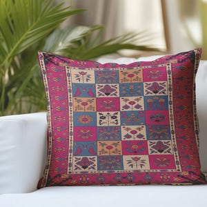 Puede incluir: Un cojín cuadrado decorativo con un diseño estampado colorido. El cojín presenta una cuadrícula de cuadrados rosas, azules, beiges y verdes, con motivos florales y geométricos. Se coloca sobre un sofá blanco, lo que sugiere decoración del hogar. Mide aprox. 40 cm x 40 cm.