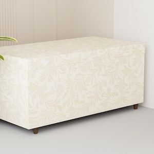 Puede incluir: Un baúl de almacenamiento de color crema con un patrón floral. El baúl tiene una base de madera y está sentado en un suelo blanco.