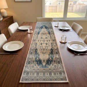 May include: A rectangular table runner featuring a central blue and beige medallion pattern with intricate geometric and floral motifs. The runner is positioned lengthwise down the center of a dark wood dining table, showcasing a symmetrical design.