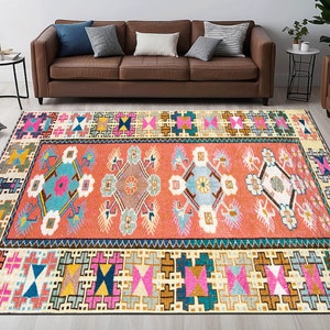 May include: A colorful, geometric rug with a central design of stylized flowers and a border of repeating geometric patterns. The rug is in shades of pink, blue, green, yellow, and brown.