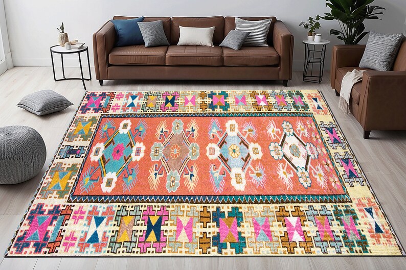 May include: A colorful, geometric rug with a central design of stylized flowers and a border of repeating geometric patterns. The rug is in shades of pink, blue, green, yellow, and brown.