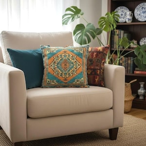 May include: A beige upholstered armchair featuring three decorative throw pillows. One pillow is solid teal, one features a central orange and teal geometric medallion pattern, and the third has a dark red and brown multi-coloured patterned design.