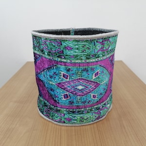 May include: A cylindrical fabric storage bin with a colorful geometric pattern in shades of green, blue, and purple. The bin has a white trim around the top edge.